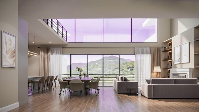 living area featuring a towering ceiling, wood finished floors, a fireplace, baseboards, and a mountain view