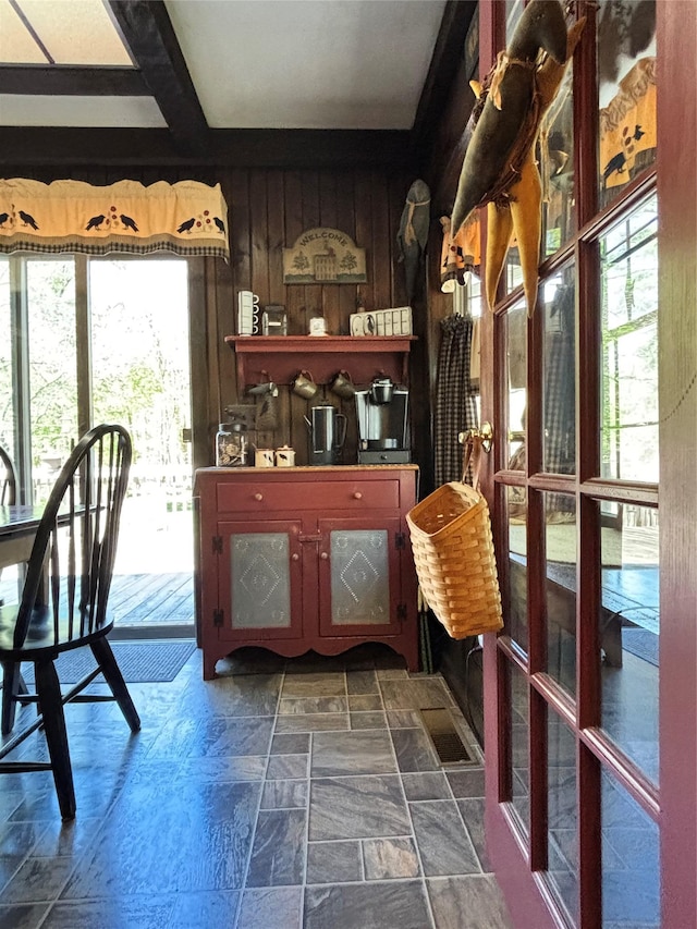 dining area with stone tile flooring, wood walls, and beamed ceiling