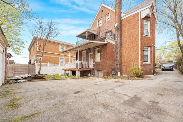 back of house featuring fence, brick siding, a porch, cooling unit, and a balcony