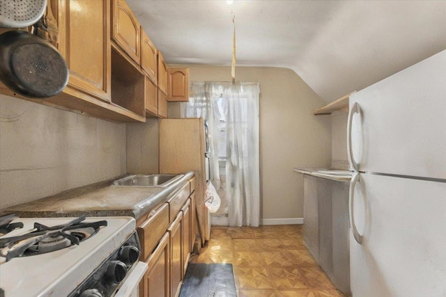 kitchen featuring brown cabinetry, a sink, baseboards, lofted ceiling, and white appliances
