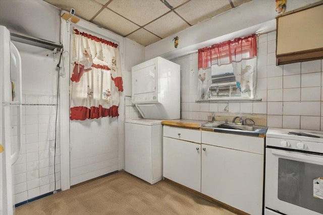 kitchen with electric range, light carpet, light countertops, stacked washing maching and dryer, and a paneled ceiling