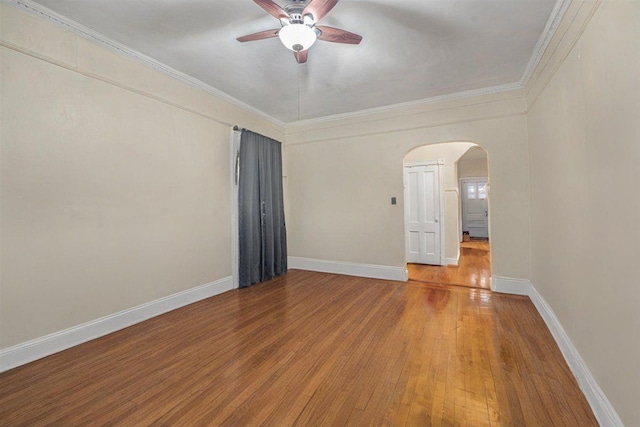 spare room with crown molding, wood finished floors, baseboards, ceiling fan, and arched walkways