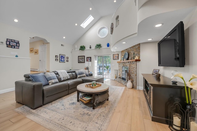 living room with baseboard heating, high vaulted ceiling, a stone fireplace, recessed lighting, and light wood-type flooring