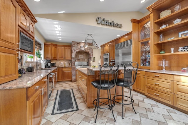 kitchen featuring light stone counters, a sink, built in appliances, a breakfast bar area, and a center island