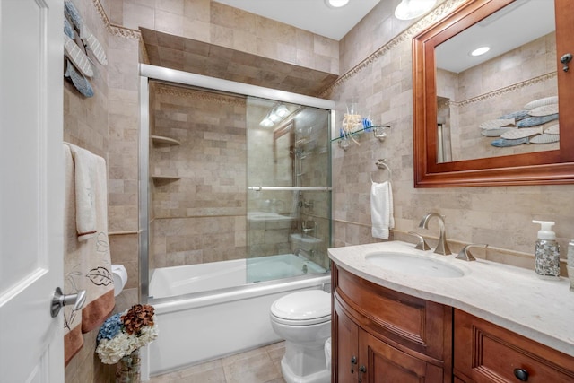 bathroom with vanity, toilet, shower / bath combination with glass door, tile walls, and tile patterned floors