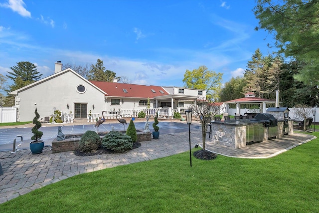 back of property featuring a lawn, a patio area, exterior kitchen, and fence