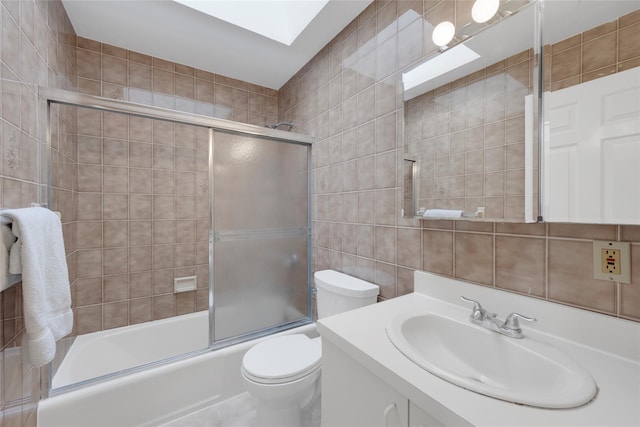full bathroom featuring vanity, toilet, tile walls, a skylight, and bath / shower combo with glass door