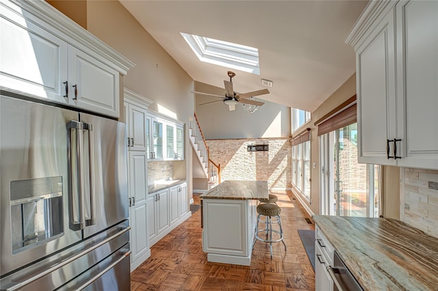 137 Melbury Rd, Babylon, NY 11702 - kitchen with stainless steel refrigerator with ice dispenser, a skylight, a kitchen breakfast bar, white cabinets, and light stone countertops