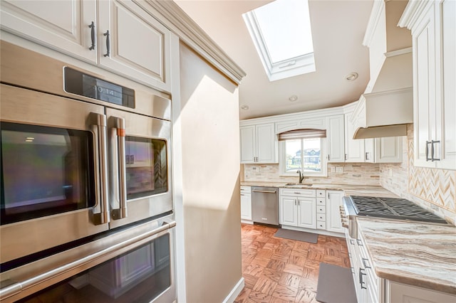 137 Melbury Rd, Babylon, NY 11702 - kitchen with appliances with stainless steel finishes, a skylight, decorative backsplash, white cabinetry, and custom range hood