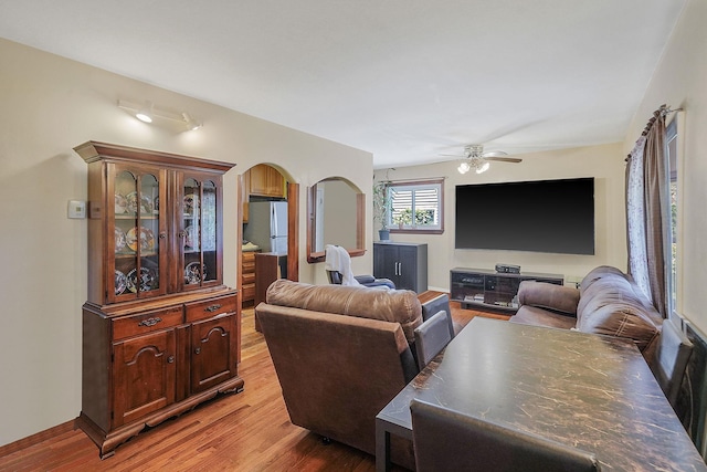 living area with arched walkways, a ceiling fan, and light wood finished floors