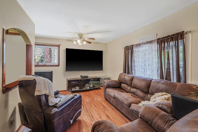 living area with arched walkways, ceiling fan, and light wood-style flooring