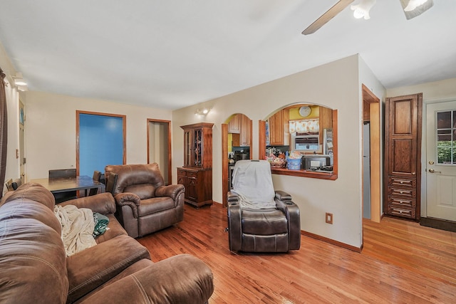living room with arched walkways, baseboards, a ceiling fan, and light wood finished floors