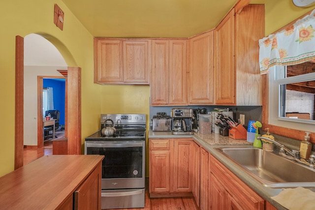 kitchen featuring light brown cabinetry, stainless steel electric range, a sink, light wood finished floors, and arched walkways