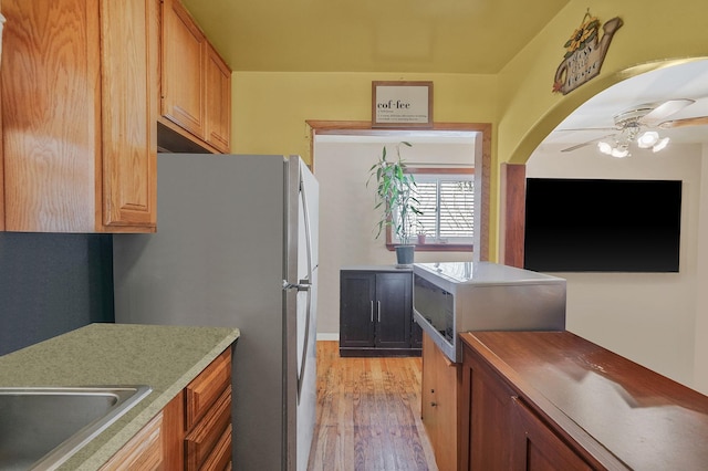 kitchen featuring freestanding refrigerator, ceiling fan, light countertops, a sink, and light wood finished floors