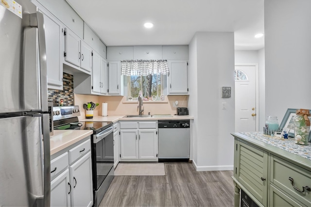 kitchen with a sink, appliances with stainless steel finishes, wood finished floors, and white cabinets