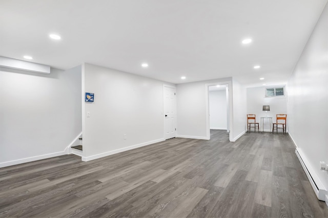 finished below grade area featuring wood finished floors, stairway, baseboards, a baseboard radiator, and recessed lighting