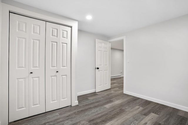 unfurnished bedroom with baseboards, a baseboard heating unit, dark wood-style floors, and a closet