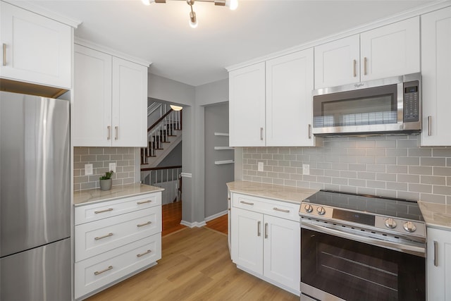 149 King St Unit 15, Chappaqua, NY 10514 - kitchen with appliances with stainless steel finishes, backsplash, light wood-style floors, and white cabinetry