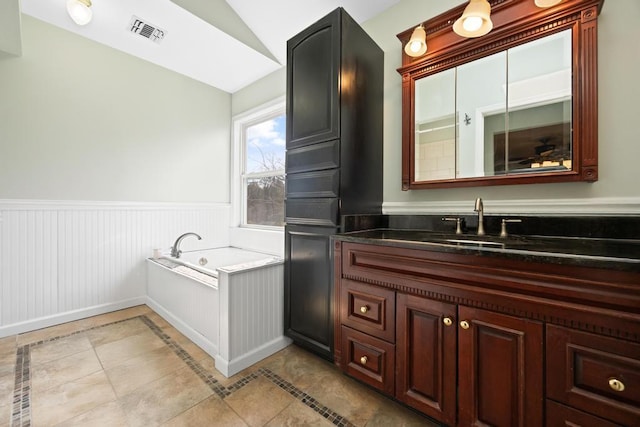 full bathroom with a bath, visible vents, wainscoting, vanity, and lofted ceiling
