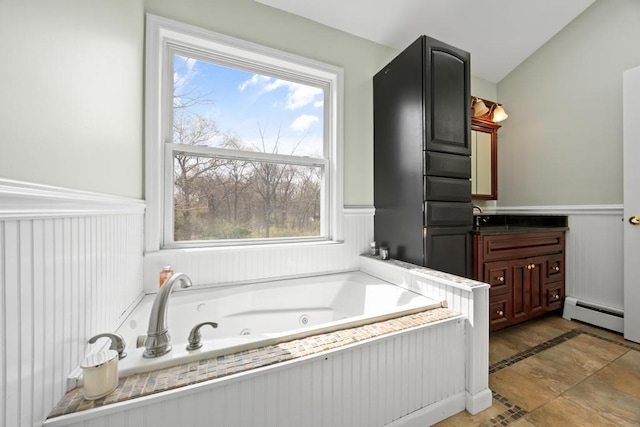 full bath with a wainscoted wall, baseboard heating, vanity, and a tub with jets