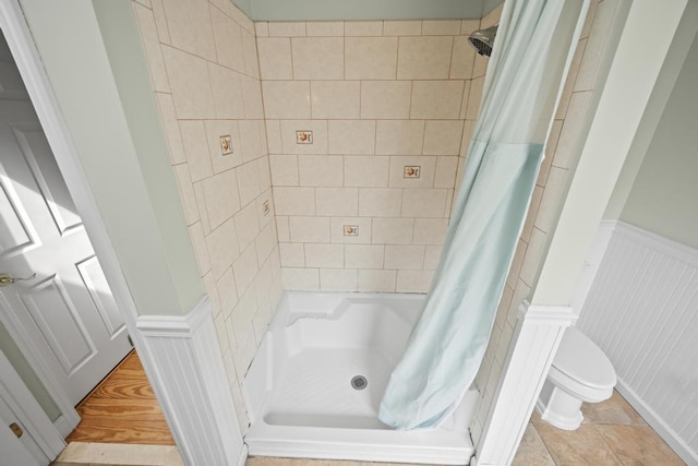 bathroom featuring a decorative wall, wainscoting, toilet, and curtained shower