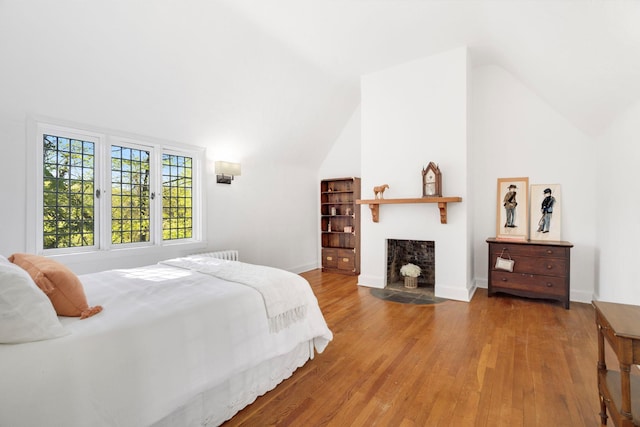 bedroom featuring baseboards, high vaulted ceiling, a fireplace with flush hearth, and wood finished floors
