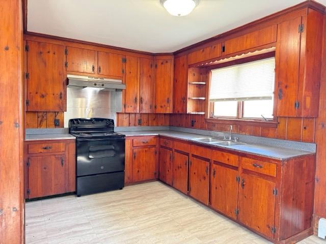 kitchen featuring black electric range, brown cabinetry, under cabinet range hood, and a sink