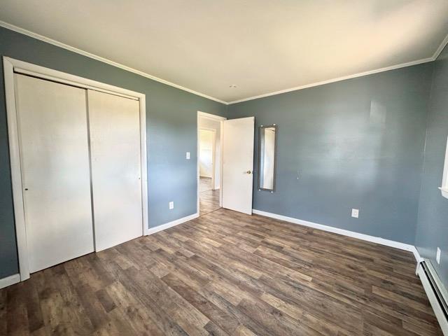 unfurnished bedroom featuring wood finished floors, baseboards, crown molding, and a baseboard heating unit