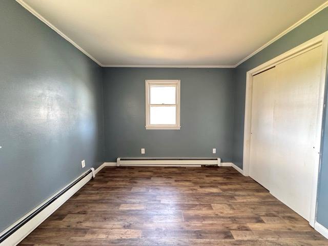 interior space with a baseboard heating unit, ornamental molding, baseboard heating, and wood finished floors