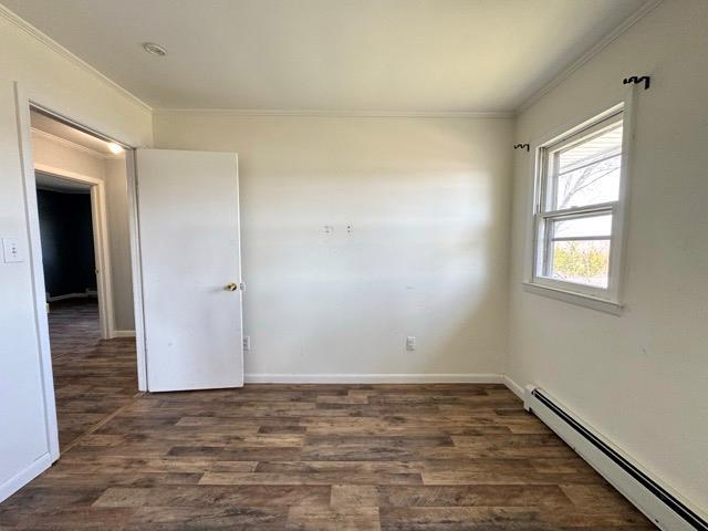 spare room featuring baseboards, ornamental molding, baseboard heating, and dark wood-type flooring