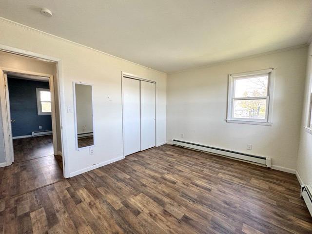 unfurnished bedroom featuring a baseboard radiator, ornamental molding, a closet, and wood finished floors