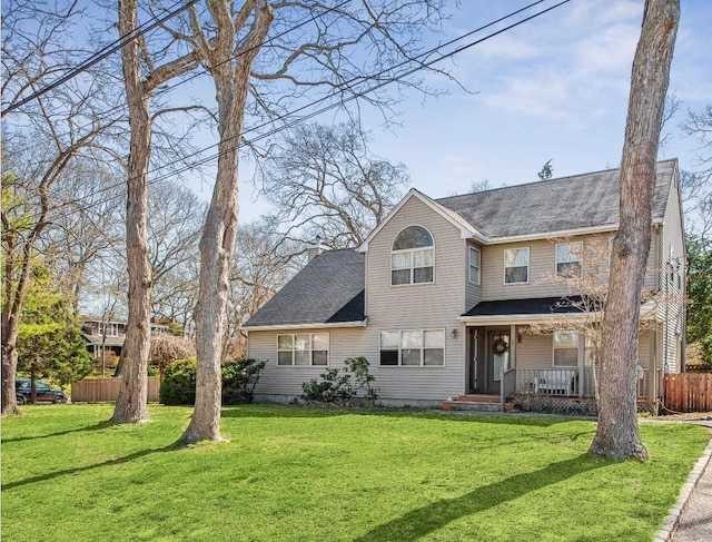 traditional home featuring a porch, roof with shingles, fence, and a front yard