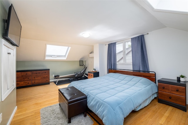 bedroom with vaulted ceiling with skylight, light wood-style floors, and a wall unit AC