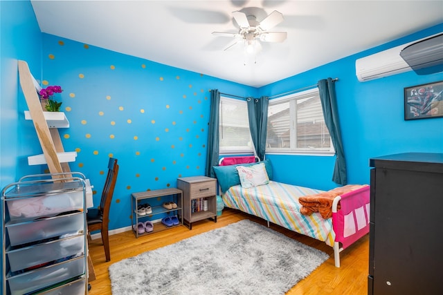 bedroom featuring baseboards, ceiling fan, a wall mounted AC, and wood finished floors