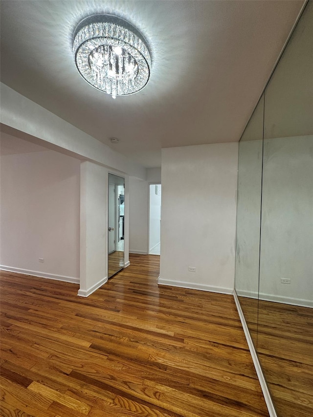 spare room featuring baseboards, a chandelier, and wood finished floors