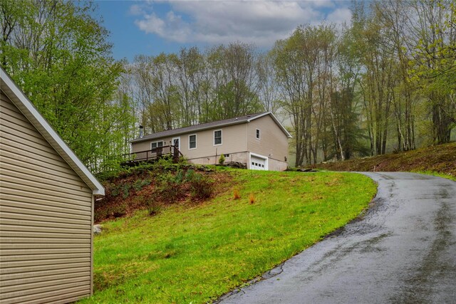 view of side of property with an attached garage, a deck, a yard, and driveway