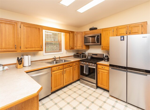 kitchen featuring stainless steel appliances, a sink, light countertops, vaulted ceiling, and light floors