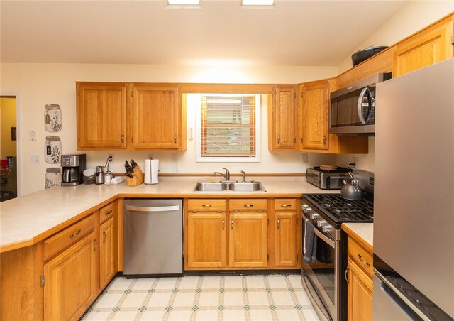 kitchen featuring appliances with stainless steel finishes, a sink, a peninsula, light countertops, and light floors