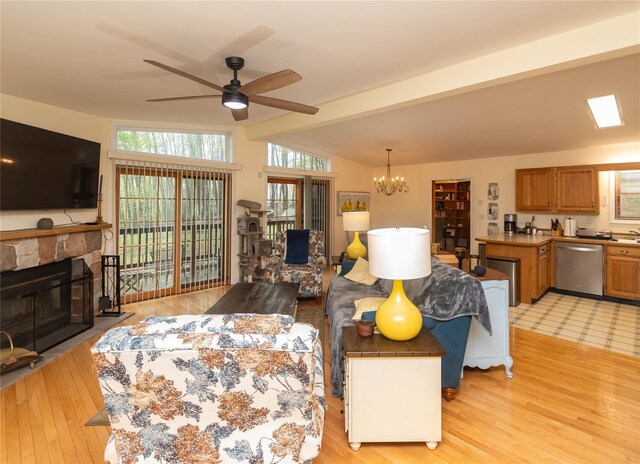 living room featuring ceiling fan, light wood finished floors, a stone fireplace, and plenty of natural light