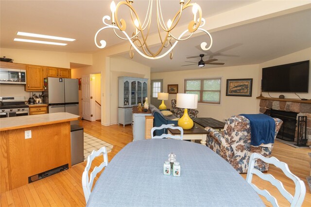 dining area with lofted ceiling, a ceiling fan, a chandelier, light wood-style flooring, and a stone fireplace