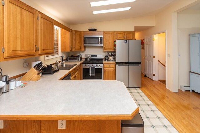 kitchen with stainless steel appliances, vaulted ceiling, light countertops, a peninsula, and brown cabinets