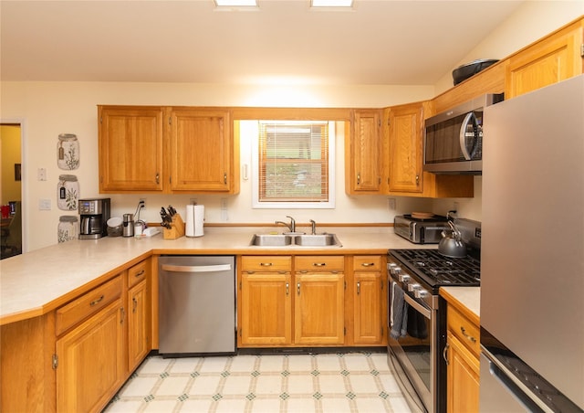 kitchen featuring appliances with stainless steel finishes, a sink, a peninsula, light countertops, and light floors