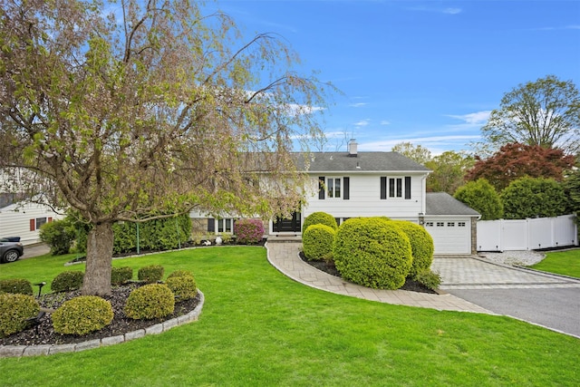 view of front facade with a gate, fence, a front lawn, a chimney, and decorative driveway