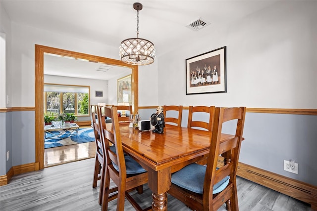 dining space with an inviting chandelier, baseboards, light wood-type flooring, and visible vents