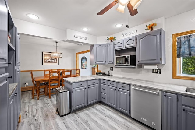 kitchen featuring a peninsula, light wood finished floors, ceiling fan with notable chandelier, gray cabinetry, and appliances with stainless steel finishes