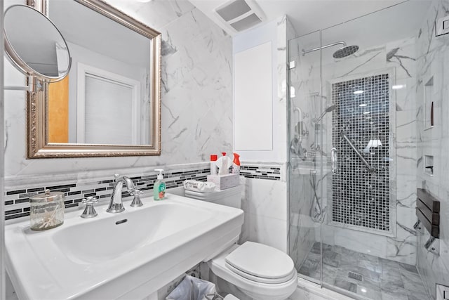 bathroom with tile walls, toilet, a marble finish shower, and a sink