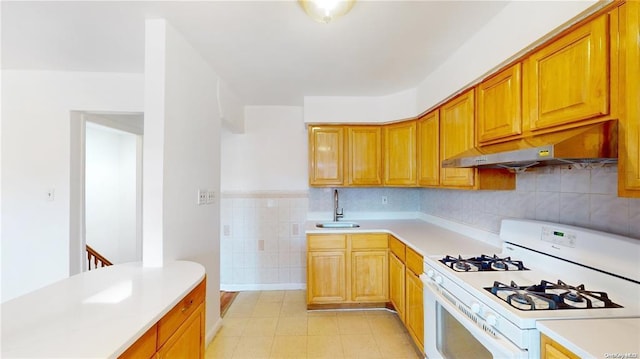 kitchen with tile walls, light countertops, a sink, white range with gas cooktop, and under cabinet range hood