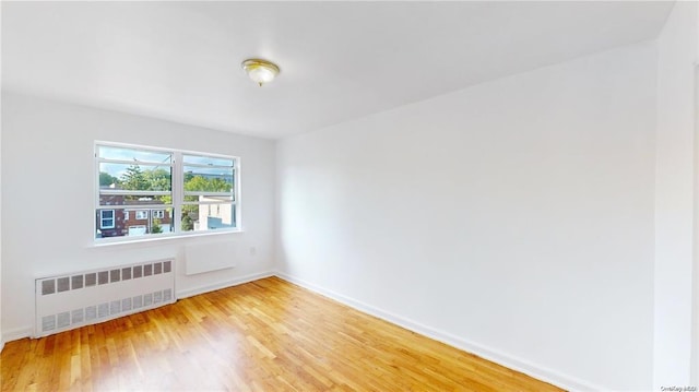 spare room featuring baseboards, radiator heating unit, and light wood-type flooring