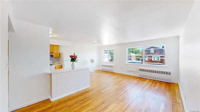 unfurnished living room featuring baseboards, light wood finished floors, and radiator