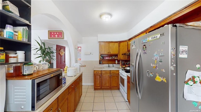 kitchen with brown cabinetry, appliances with stainless steel finishes, a sink, light tile patterned floors, and light countertops